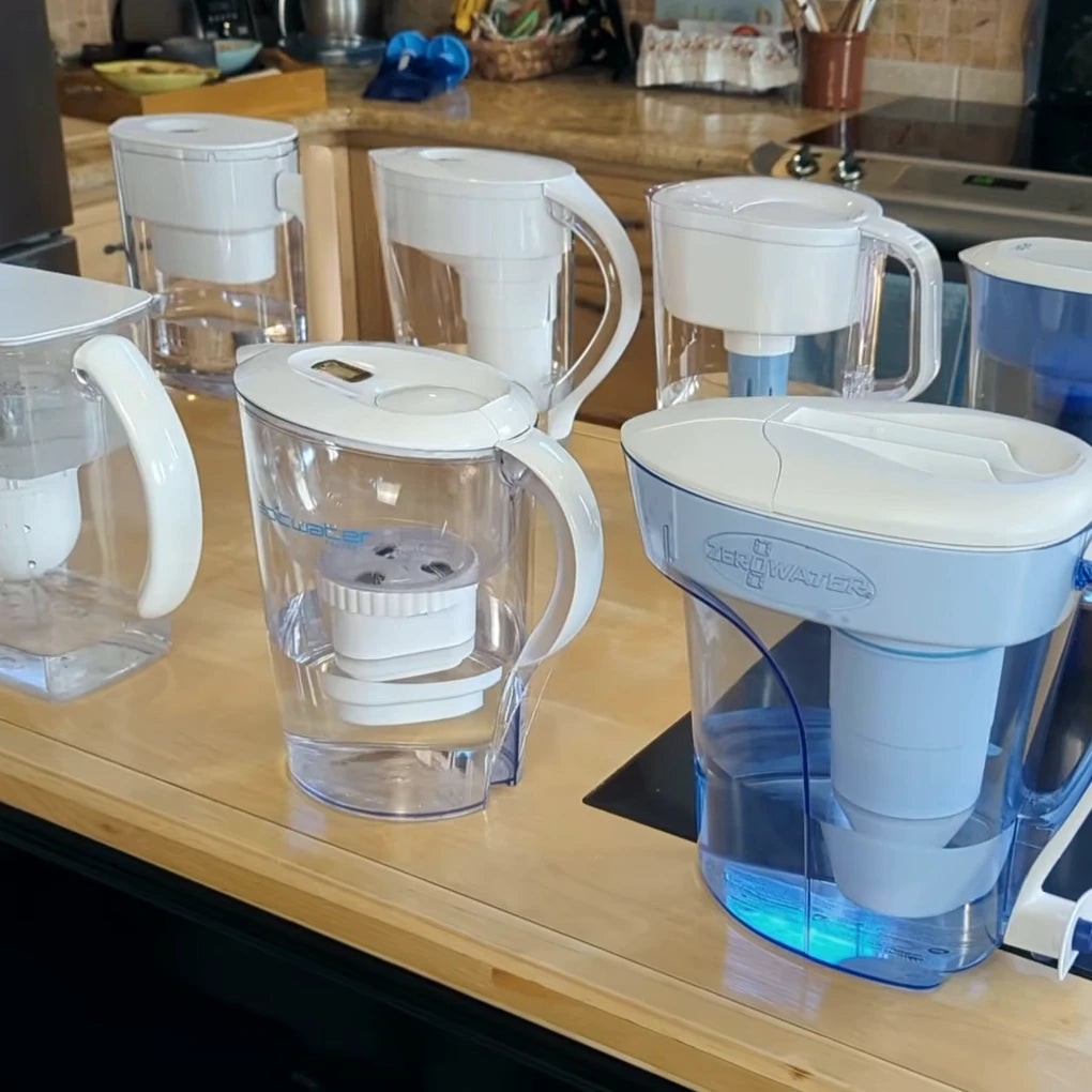 Eight plastic filter pitchers lined up on a kitchen counter